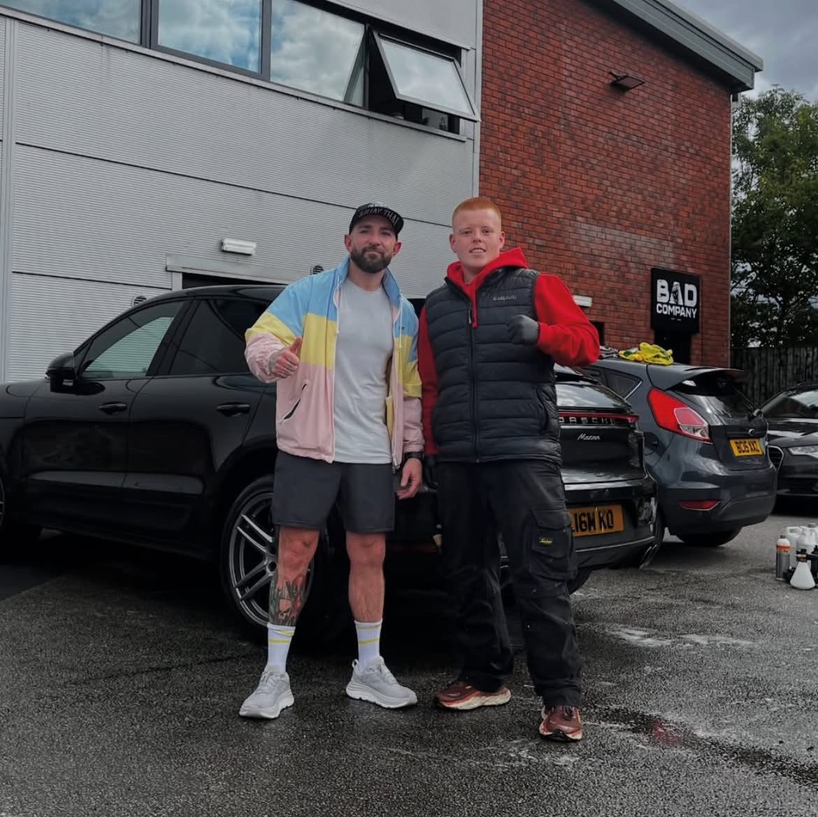 Sam with Liam Harrison in front of a black Porsche Macan at Bad Company gym in Leeds